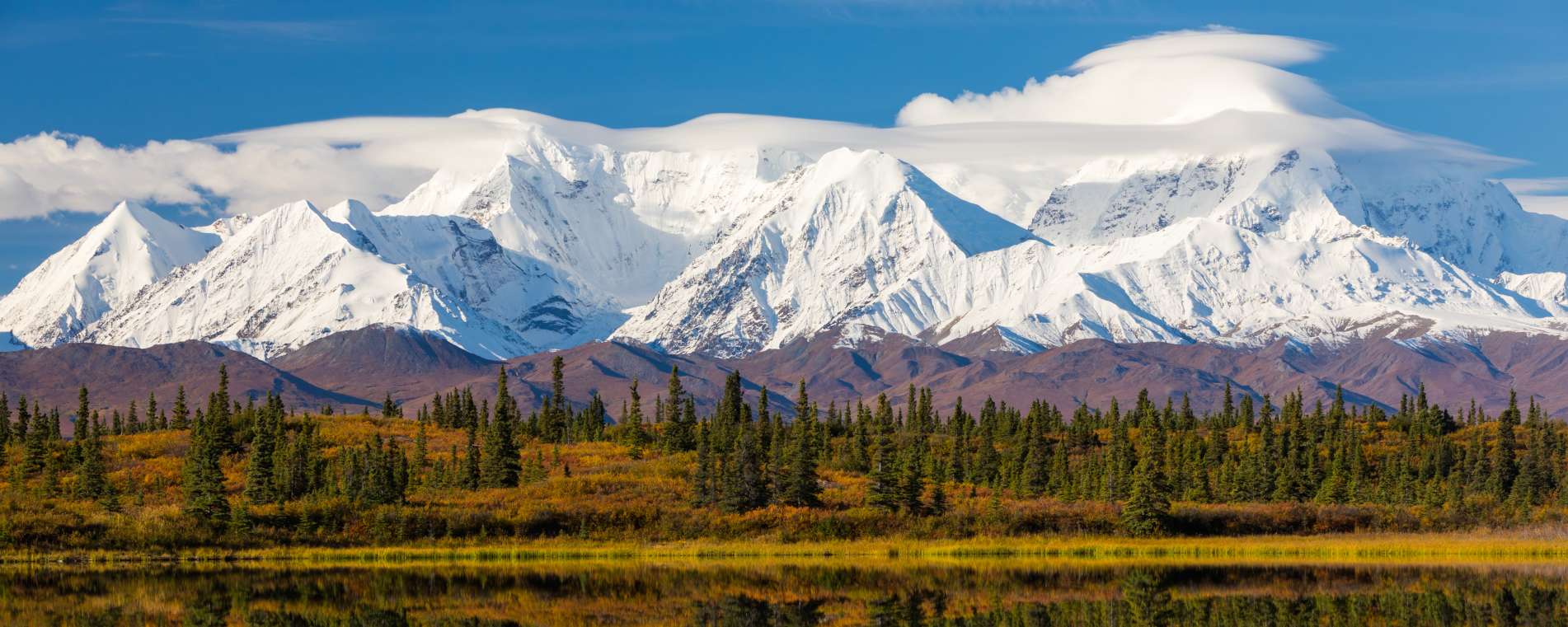 Snow covered mountains, blue sky, and reflection of landscape on lake