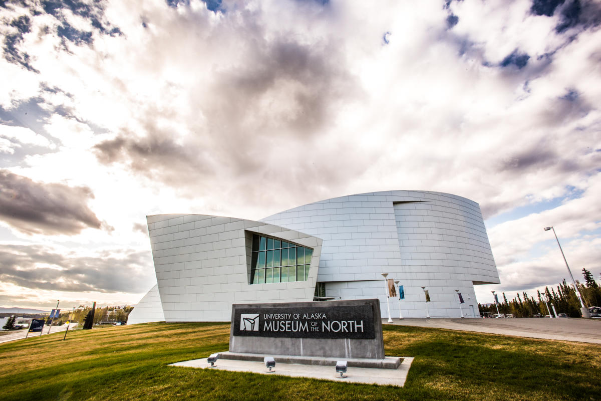 Modern exterior of the Museum of the North, featuring sleek, curved architecture and a large sign on the lawn under a cloudy sky