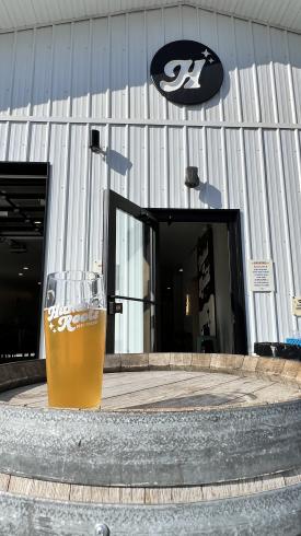 A glass of beer from Humble Roots sits on a wooden barrel outside a taproom.