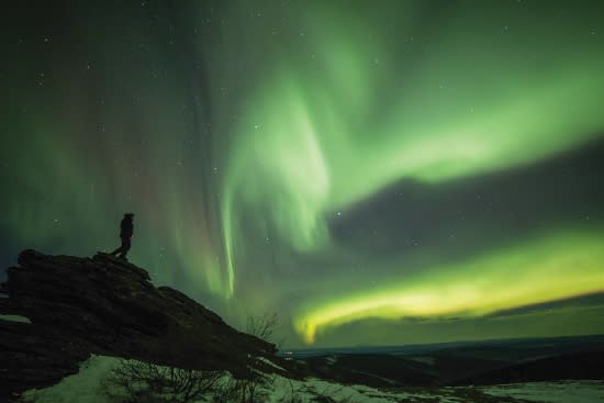 Person standing on rock looking at aurora over Murphy Dome