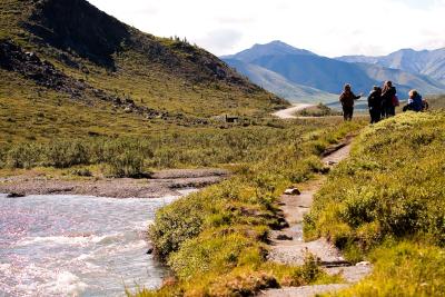 Four people walking on a trail next to a river