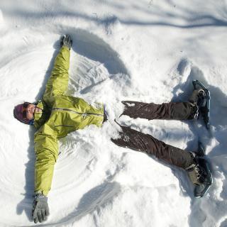 Person laying on ground in the snow, making a snow angel.